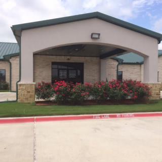 A modern building entrance with manicured landscaping and a parking area.