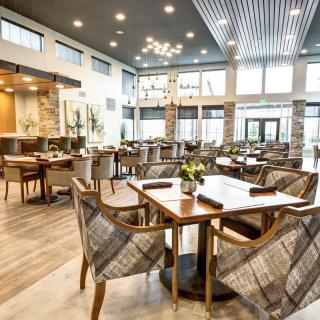 A modern restaurant interior with elegantly arranged tables and chairs, featuring a warm wooden floor and stylish lighting.
