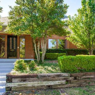 A charming house with brick exterior and well-maintained landscaping, featuring lush greenery in the front yard.