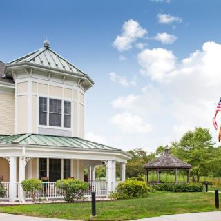 A two-story building with a gazebo and an American flag in a landscaped area under a blue sky.