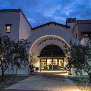 A well-lit building entrance at dusk with surrounding trees.