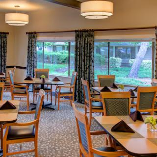 A well-lit dining area featuring wooden tables and chairs, enhanced by large windows overlooking a green view.