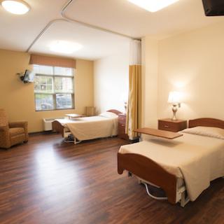 A well-lit hospital patient room featuring two beds and cozy furniture.