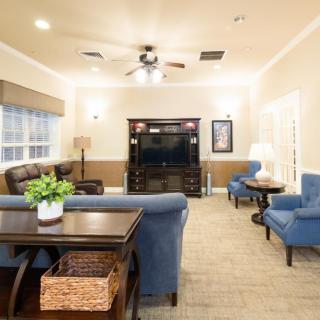 A cozy living room with blue armchairs and a comfortable sofa, centered around a TV stand under a ceiling fan.