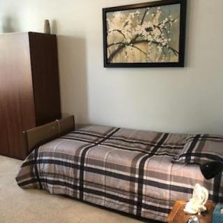 A cozy bedroom featuring a neatly made bed, decorative art on the wall, and simple furniture.