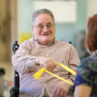 An elderly man smiling while participating in a therapy exercise session.