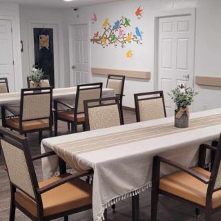 A neatly arranged dining room with tables covered in cloths, surrounded by chairs and decorated with potted plants.