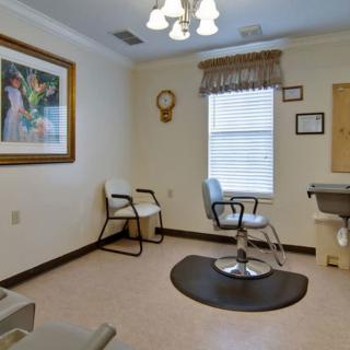 A hair salon interior featuring a single styling chair, a waiting area with chairs, and decorative artwork on the walls.