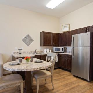 A modern kitchen and dining area with a table set for two, featuring dark wooden cabinets and stainless steel appliances.