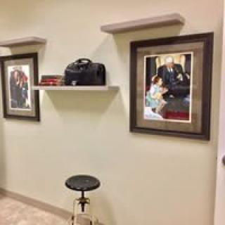 A room interior featuring framed artwork on the wall, a small shelf with items, and a stool beneath.