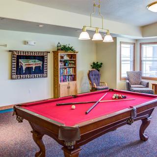 A cozy recreation room featuring a red felt pool table with cues, surrounded by comfortable seating and decor.