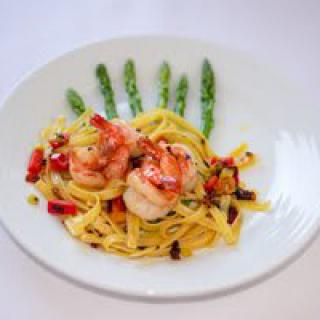 A gourmet dish featuring pasta and shrimp, garnished with asparagus and vegetables.