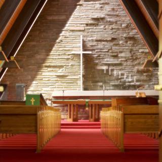 A serene church interior featuring wooden pews and an altar with a prominent cross.