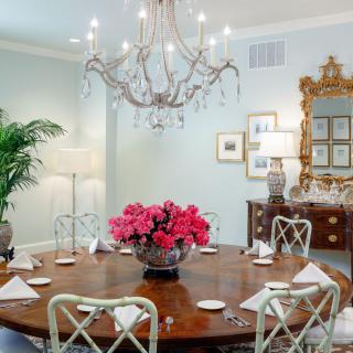 An elegantly decorated dining room featuring a chandelier, round table with flowers, and classic furnishings.