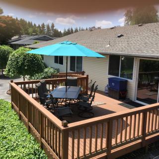 A cozy backyard deck with a table and chairs, shaded by a blue umbrella.