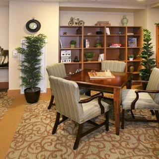 An elegant office meeting area with a table, chairs, bookshelf, and decorative plants.
