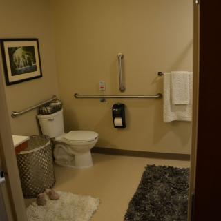 A clean and organized bathroom featuring a toilet, a towel rack, a laundry basket, and wall art.