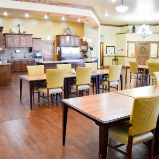A spacious and well-lit dining area with wooden tables and chairs, connected to a kitchen space.