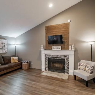 A cozy living room with a fireplace, sofa, and television, featuring modern decor and wood flooring.