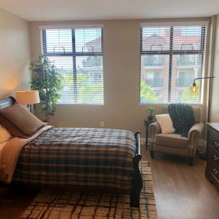 A cozy bedroom with a plaid bedspread, large windows, and comfortable seating.