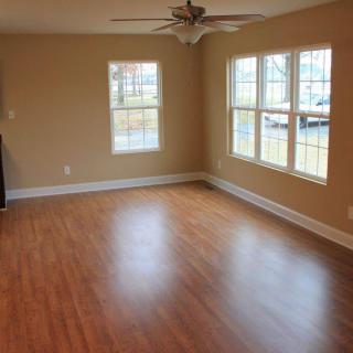 A spacious empty room with wooden flooring, large windows, and a ceiling fan.