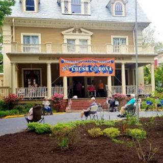 Community gathering at a historic house, featuring an outdoor stage and attendees enjoying the event.