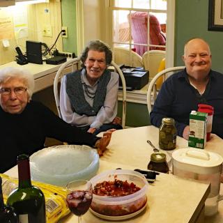 A group of three people sitting at a table with food and drink items in a cozy kitchen setting.