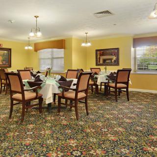 A well-appointed dining room with neatly arranged tables and chairs, featuring elegant lighting and patterned carpet.