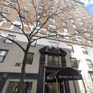 The exterior of a tall urban building with a tree in front and an entrance canopy.
