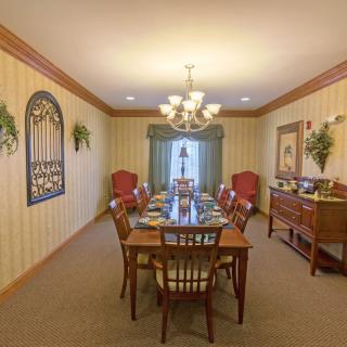 A traditionally decorated dining room with a long table, multiple chairs, and a chandelier overhead.