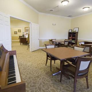 A well-lit room featuring a piano, multiple tables and chairs, and a bookshelf.