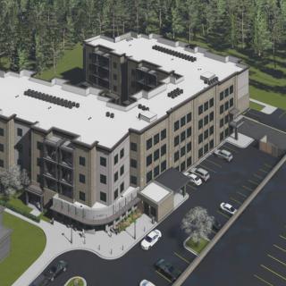 A bird's-eye view of a modern multi-story building surrounded by a forest with an adjacent parking lot.