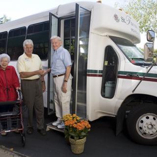 Elderly individuals standing next to a community transport bus.