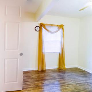 An empty room with hardwood flooring and yellow curtains.