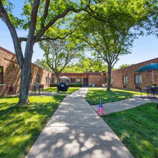A serene courtyard with lush green trees and a paved pathway surrounded by brick buildings.