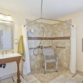An accessible bathroom with a roll-in shower, equipped with grab bars and a shower chair.