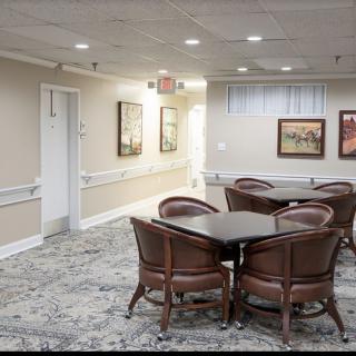 A quiet room with upholstered chairs and tables, decorated with paintings and carpeted flooring.
