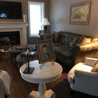 A cozy living room with a couch, chairs, a table with a framed photograph, and a fireplace.
