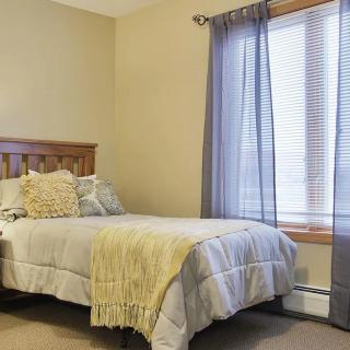 A cozy bedroom with a bed adorned with pillows and a throw, featuring a window with curtains.