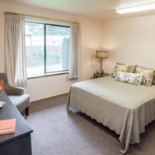 A cozy bedroom with a neatly made bed, a window allowing natural light, and simple, neutral decor.