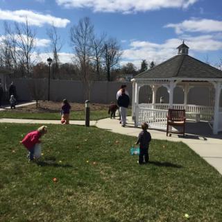 Children play on the grass near a gazebo on a sunny day.