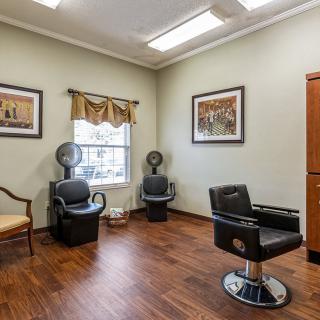 A well-lit salon with a barber chair and hairdryer chairs, featuring wood flooring and wall art.