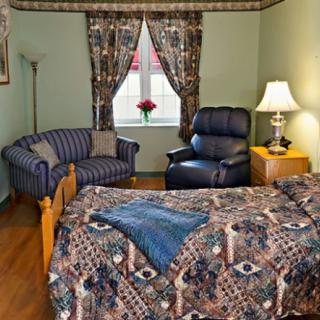 A cozy bedroom with patterned curtains and bedding, featuring a comfortable armchair and a small loveseat.