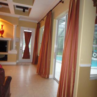 A modern living room with large windows overlooking a pool, featuring elegant curtains and stylish decor.