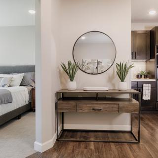 A contemporary bedroom features a stylish console table with plants and a round mirror, complemented by wood flooring.
