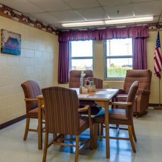 A small meeting room with a table, surrounded by chairs and featuring windows with curtains.