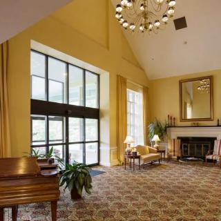 A spacious and elegantly designed living room featuring a piano, chandelier, fireplace, and large windows.