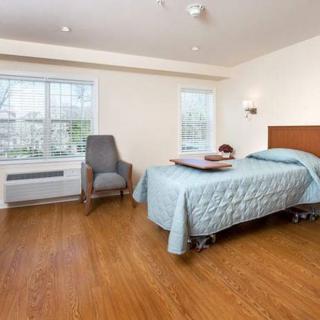 A minimalist bedroom with a hospital bed, chair, and large windows.