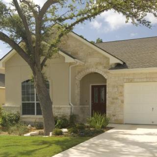 A suburban house with a tree in the front yard and a spacious driveway.