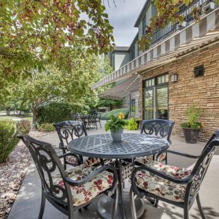 A cozy outdoor patio with a table and cushioned chairs surrounded by lush greenery.